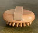 A wooden massage brush with spherical protrusions on a flat surface, with a fabric handle.
