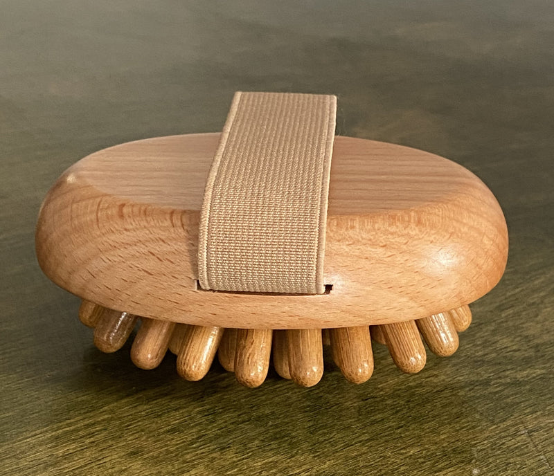 A wooden massage brush with spherical protrusions on a flat surface, with a fabric handle.