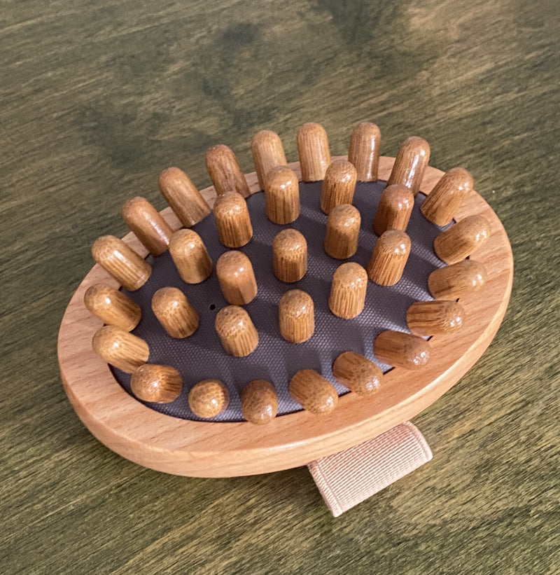 A wooden massage brush with spherical protrusions on a flat surface, with a fabric handle.
